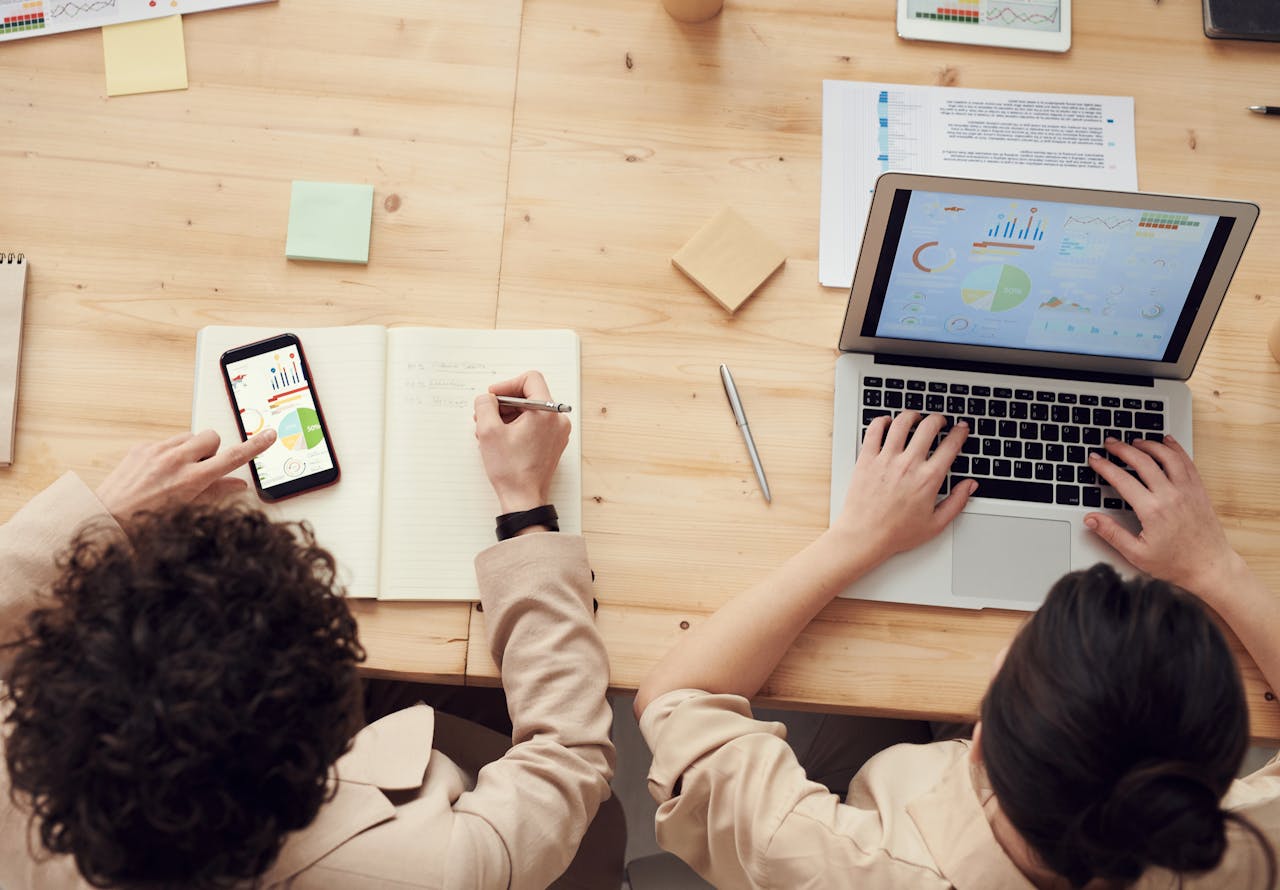 Overhead shot of two colleagues collaborating with devices and notes in a business meeting.